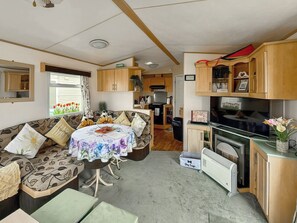 Interior compacto de una caravana con zona de comedor, kitchenette y espacio de estar con sofá y mesa.