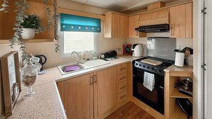 A compact kitchen with wooden cabinets, a sink, a stove, and a window with blinds.