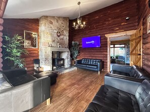 A log cabin interior with a stone fireplace, leather sofas, a mounted television, and wooden walls. - Bellstane Chalet - UKC9440 (Glasgow)