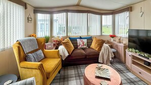 Ein Wohnzimmer mit gelber Couch, braunem Sofa, einem runden Couchtisch und einem Fernseher.