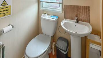 A bathroom with a toilet, sink, and trash bin. There is a caution sign on the wall.