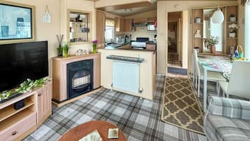 Un espacio habitable pequeño con televisión, chimenea, cocina, comedor y una alfombra estampada.