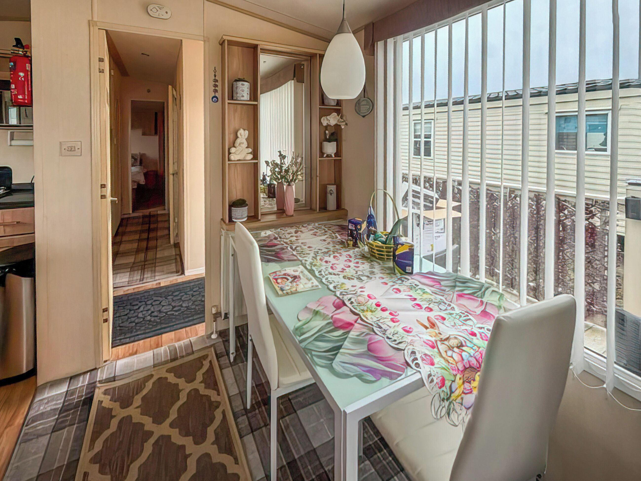 Un comedor con una mesa dispuesta para dos, una cocina al fondo y vistas amplias a través de grandes ventanales.