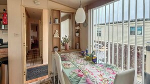 Ein Essbereich mit Tisch für zwei Personen, eine Küche im Hintergrund und Blick durch große Fenster.