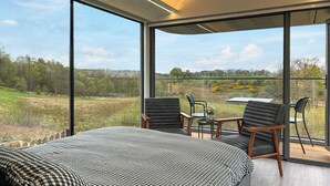 Un dormitorio con una cama grande, dos sillones, una mesa y un balcón con vistas a un paisaje verde.