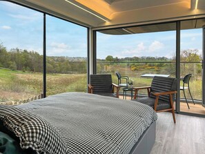 A bedroom with a large bed, two chairs, a table, and a balcony with a view of a green landscape. - 1 bedroom accommodation in Glasgow (Glasgow)