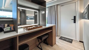 Una habitación de hotel moderna con un escritorio de madera, un espejo, una pequeña zona de estar y una puerta.