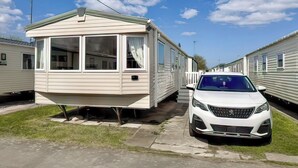 Ein Wohnmobil mit geparktem Auto davor, wolkenloser Himmel und eine Rasenfläche.