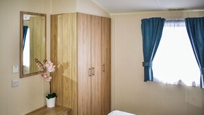 Une chambre à coucher avec une armoire en bois, une table de chevet ornée d’un vase de fleurs, un lit et une fenêtre avec des rideaux.