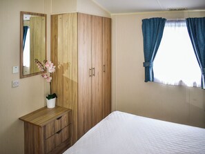 Ein Schlafzimmer mit einem hölzernen Kleiderschrank, einem Nachttisch mit Blumenvase, einem Bett und einem Fenster mit Vorhängen.