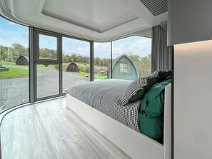 Ein Schlafzimmer mit großem Fenster, einem Bett mit kariertem Überwurf und Blick auf eine ländliche Landschaft mit kleinen Häusern.