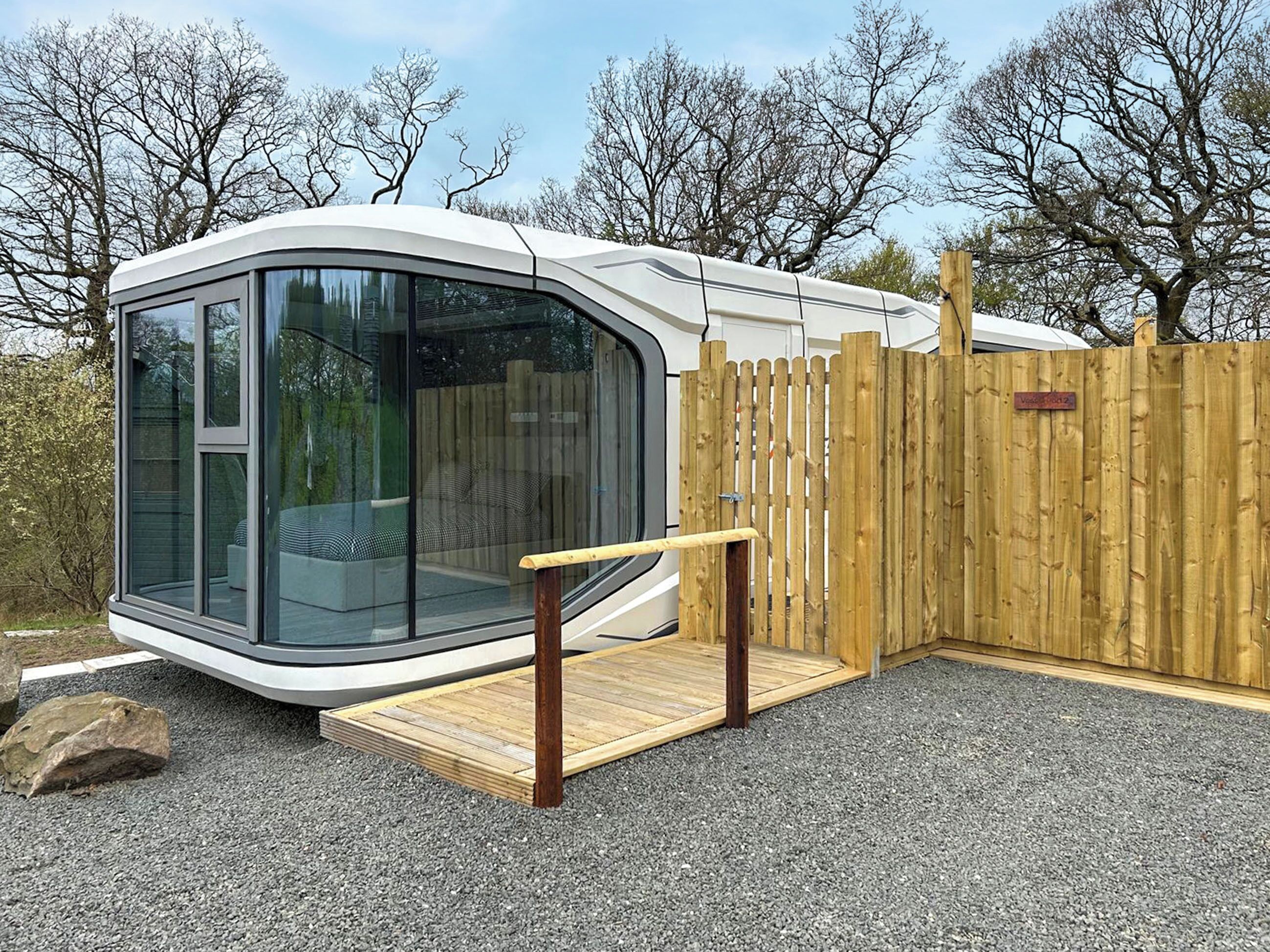 Una casa móvil moderna y compacta con un amplio ventanal, una terraza de madera y una zona vallada.