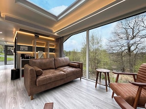 Ein modernes Interieur mit einer Ledersofa, Holzböden und einem großen Fenster mit Blick auf Bäume.