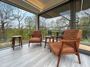 Ein modernes Interieur mit großen Fenstern, Holzböden und einer Sitzecke mit Stühlen und Tischen.