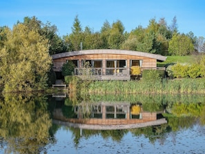 Eine hölzerne Blockhütte am Seeufer mit einer Terrasse, umgeben von Bäumen und einem ruhigen See.