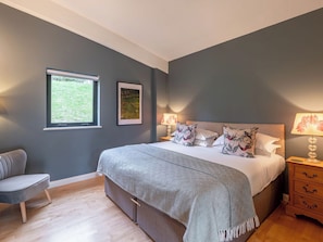 Ein Schlafzimmer mit einem Bett, Nachttischen, einem Sessel und einem Fenster.