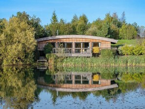 A lakeside wooden cabin with a deck, surrounded by trees and a calm lake. - 3 bedroom accommodation in Richmond (Richmond)