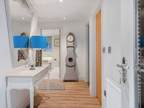 Ein Flur mit einem weißen Konsolentisch, einer blauen Lampe, einem dekorativen Spiegel, einer Wanduhr und einer Holztür.