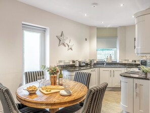 A modern kitchen with white cabinets, a granite countertop, and a dining area with striped chairs.