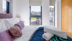 Et moderne hotelværelse med seng, puder, et tæppe og udsigt gennem en dør.