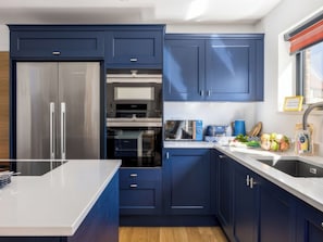 A modern kitchen with blue cabinets, a stainless steel refrigerator, a built-in oven, and a sink. - 3 bedroom accommodation in Dorchester (Dorchester)