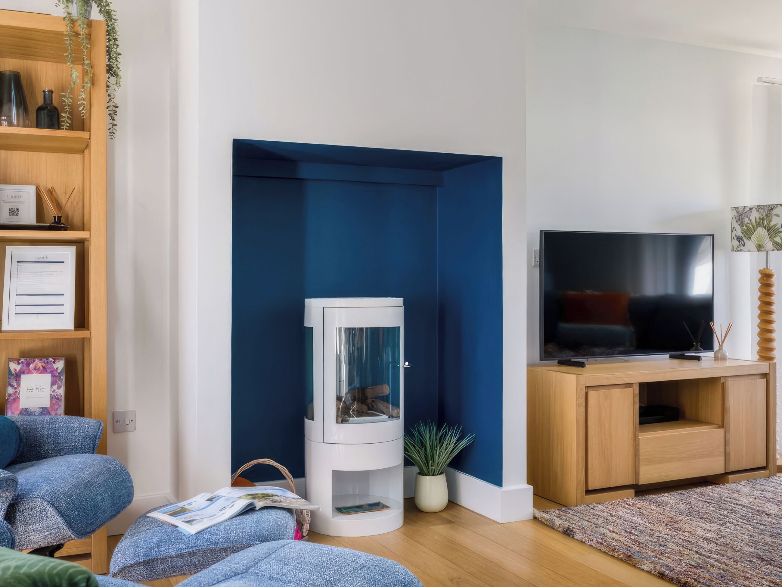Una sala de estar con televisor, un mueble blanco, una pared azul y una estantería.