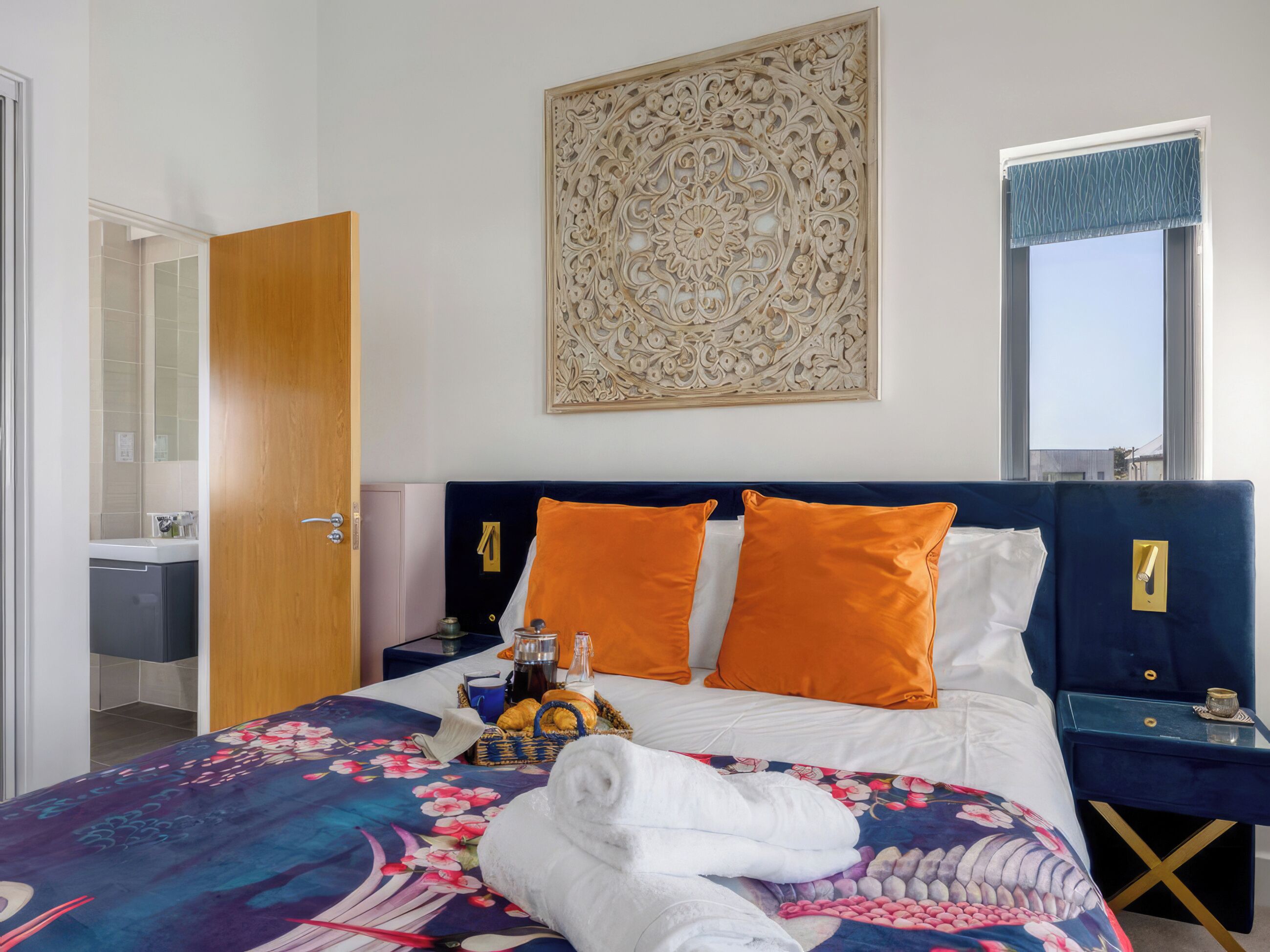 Habitación de hotel con cama, mesita de noche, ventana con vistas y puerta que da a un baño.