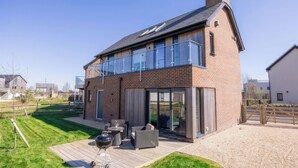 Et moderne hus med to etager, en terrasse, udendørs møbler og en grill.