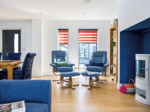 A modern living room with a wooden floor, two blue armchairs with cushions, a blue sofa, a wooden coffee table, and a bookshelf. - 3 bedroom accommodation in Dorchester (Dorchester)