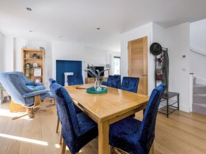 Een eetgedeelte met een houten tafel en blauwe fauteuils, een boekenkast en een televisie op de achtergrond.