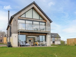 Ein modernes, zweistöckiges Haus mit Balkon, großen Fenstern und einer sichtbaren Sitzgelegenheit im Freien.
