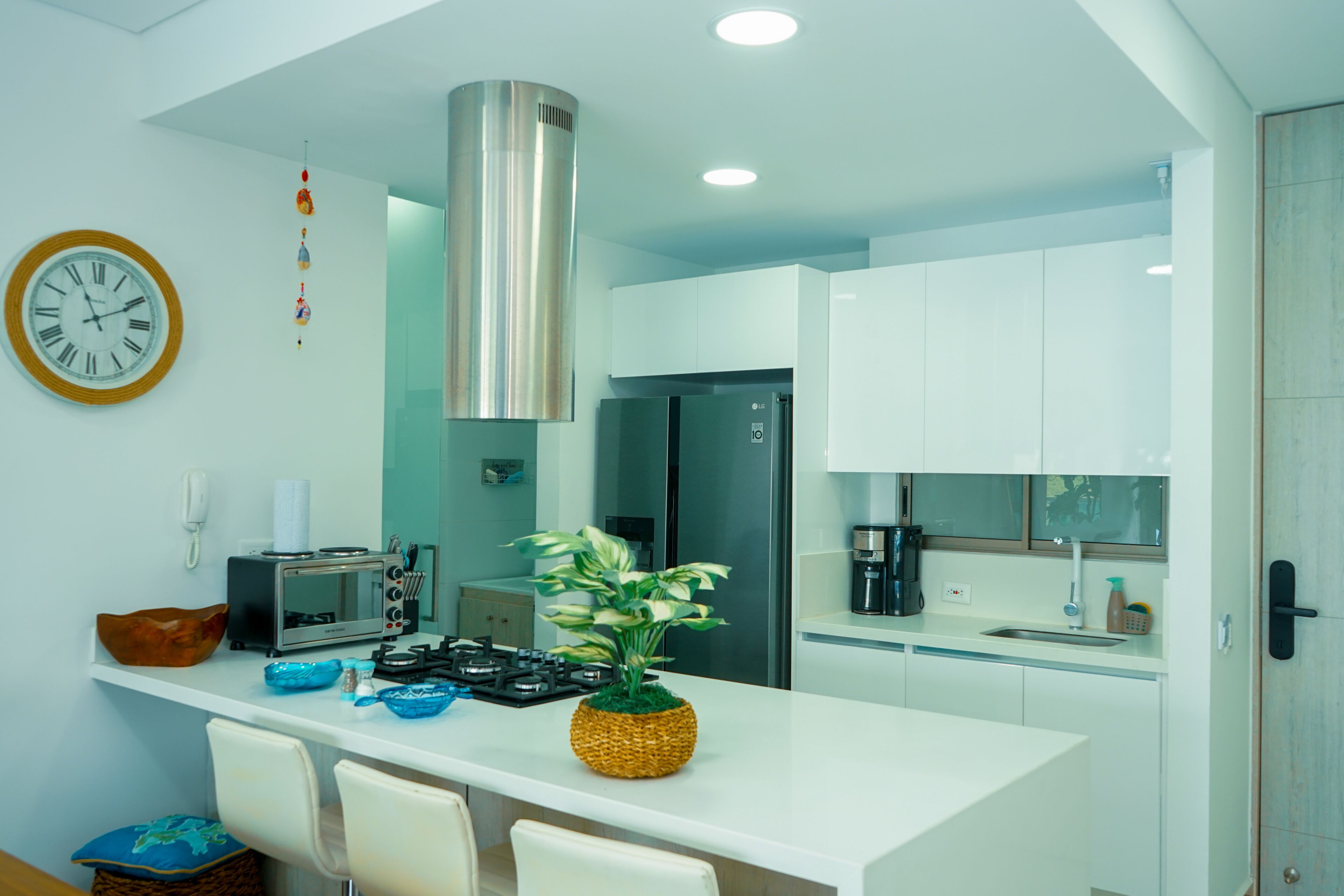 Una cucina moderna con mobili bianchi, una cappa in acciaio inossidabile, un forno a microonde e una piccola isola con sedie.