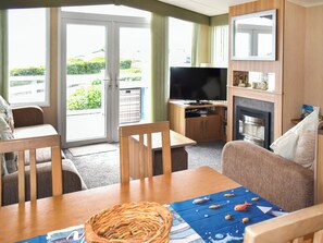 A room with a TV, a fireplace, a dining table, and a sofa. - Ivy Close 20 - UKC9401 (Exmouth)