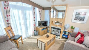Ein Wohnzimmer mit einer Couch, einem Sessel, einem Couchtisch, einem Fernseher, einem Kamin und einem Bücherregal.