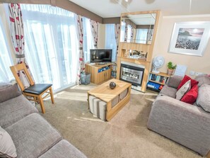 Ein Wohnzimmer mit einer Couch, einem Sessel, einem Couchtisch, einem Fernseher, einem Kamin und einem Bücherregal.