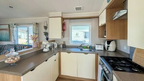 A compact kitchen with a stove, sink, and a window. - 3 bedroom accommodation in Towyn (Towyn)
