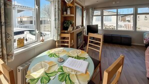 A dining area with a round table, chairs, a television, and a fireplace. - 3 bedroom accommodation in Towyn (Towyn)
