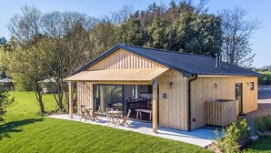 A wooden cabin with a covered patio, outdoor seating, and a gravel driveway. - 2 bedroom accommodation in Cardiff (Cardiff)