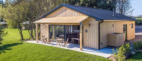A wooden cabin with a covered patio, outdoor seating, and a gravel driveway.