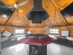 Una cabaña de madera con una mesa central, dos ventanas y un cartel que indica un lugar feliz.