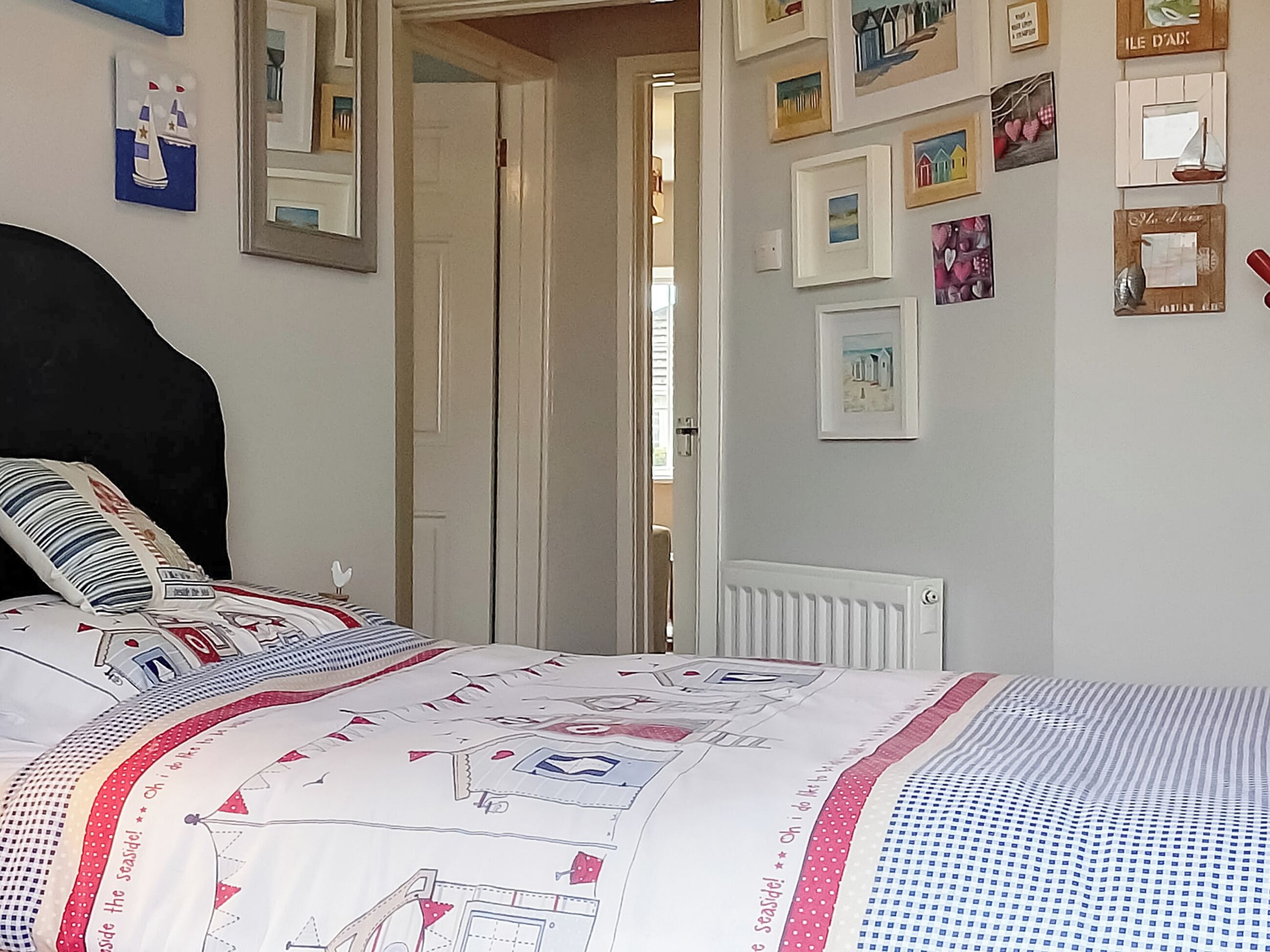 A bedroom with a bed, a door, and a wall decorated with framed pictures.