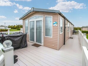 A mobile home with a covered deck, a window with a number sign, and a small outdoor seating area. - Hawks View 44 - UKC9399 (Exmouth)