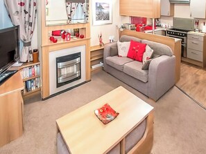 Ein gemütlicher, kompakter Wohnraum mit einer Couch, einem kleinen Tisch, einem Kamin, einem Fernseher und einer Küchenzeile.