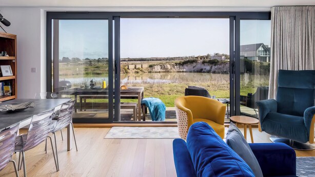 Ein modernes Wohnzimmer mit einem großen Schiebeglasfenster, das einen Blick auf ein Gewässer und die Landschaft freigibt.