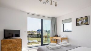 Ein modernes Hotelzimmer mit Bett, Fernseher, Schreibtisch und Blick auf ein Gewässer.
