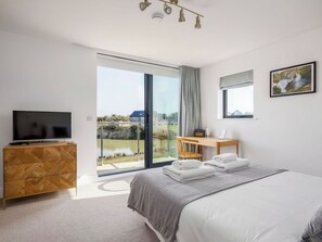 Ein modernes Hotelzimmer mit Bett, Fernseher, Schreibtisch und Blick auf ein Gewässer.