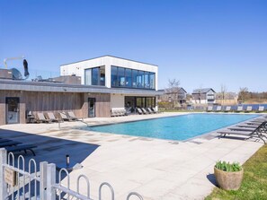 Ein modernes Gebäude mit Schwimmbad, Liegestühlen und blauem Himmel.