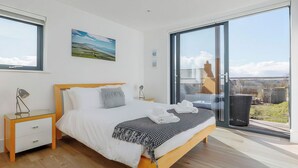 A modern bedroom with a large bed, a nightstand, a lamp, a painting, and a view through a sliding glass door. - 3 bedroom accommodation in Dorchester (Dorchester)