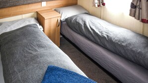 Ein Einzelbett mit Holz Kopfteil, ein kleiner Nachttisch und ein blaues Handtuch auf dem Boden.