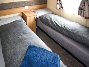 Ein Einzelbett mit Holz Kopfteil, ein kleiner Nachttisch und ein blaues Handtuch auf dem Boden.